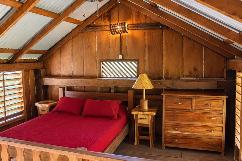 Bed with a red bedspread under the wooden roof